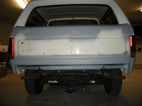 1986 Ford Bronco - The rear of a 1986 Ford Bronco shows primer on the tailgate, indicating bodywork in progress, with a trailer hitch visible below.