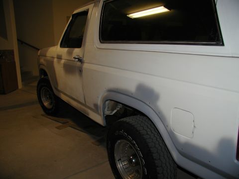 1986 Ford Bronco - Side view of a white SUV, likely a Ford Bronco, undergoing bodywork in a garage.