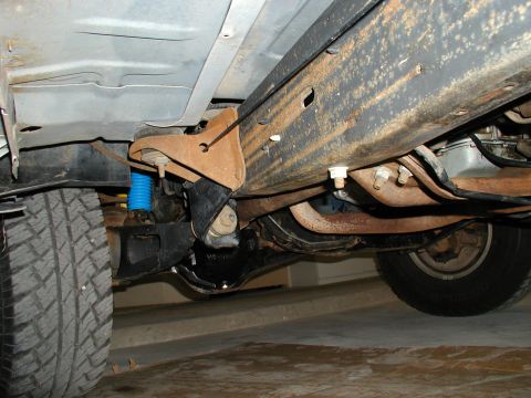 1986 Ford Bronco - The underside of a vehicle reveals its frame, suspension components, and tires, with visible signs of rust.