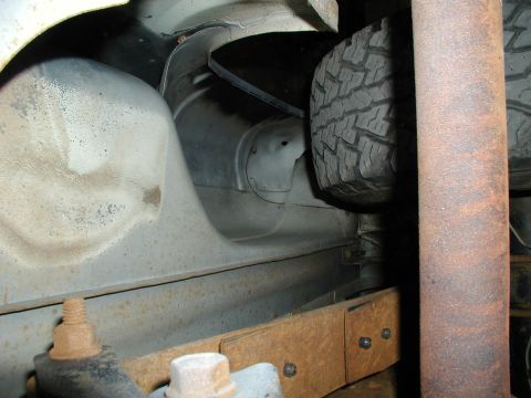 1986 Ford Bronco - The undercarriage of a vehicle reveals a spare tire, rusty exhaust, and leaf spring assembly.