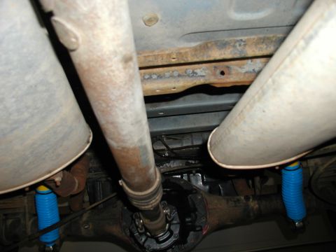 1986 Ford Bronco - The undercarriage of a vehicle shows the rear axle, driveshaft, and dual exhaust system with blue shock absorbers.