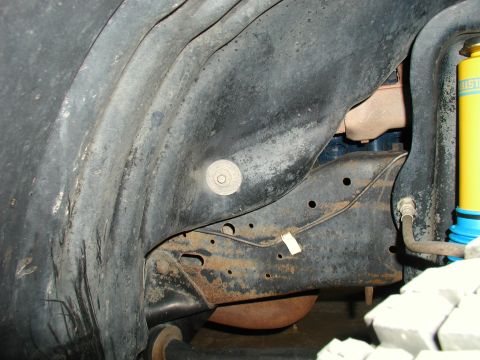 1986 Ford Bronco - Close-up view of the undercarriage frame and suspension components, including a yellow Bilstein shock absorber.
