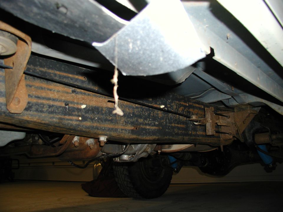 Undercarriage frame rail with rust, coil spring and tire visible