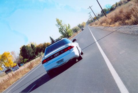 1996 Ford Probe - A white 1996 Ford Probe GT is seen from behind driving down a rural road with power lines and trees lining the way.