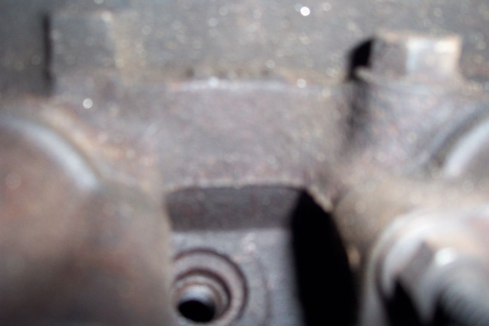 Close-up of a rusty, metallic engine component with visible bolt heads and a threaded hole