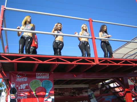 1990 Ford Bronco - Four women in checkered halter tops stand on a red-framed elevated platform above a Coca-Cola and SCORE promotional banner.