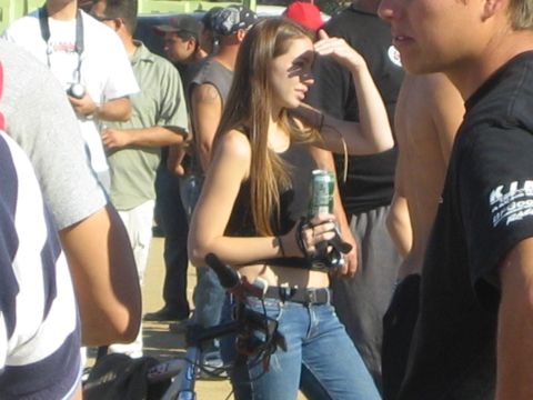 1990 Ford Bronco - woman in a black tank top and jeans holds a beer can while standing with a bicycle among a crowd of people outdoors.