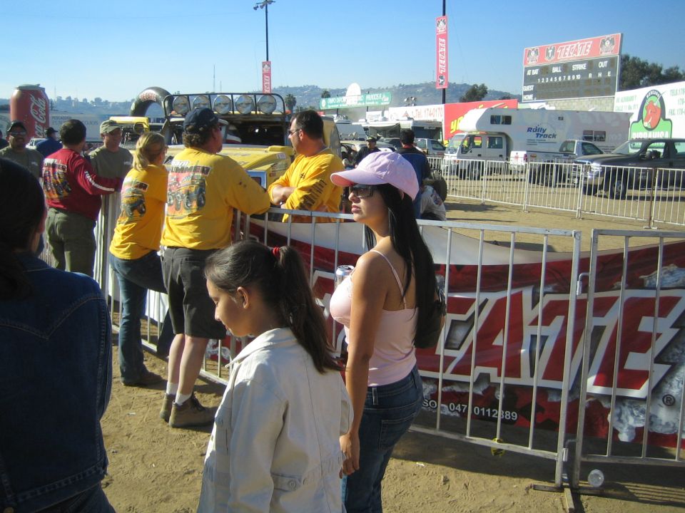 Woman in pink visor and tank top by a barricade at a dusty race venue