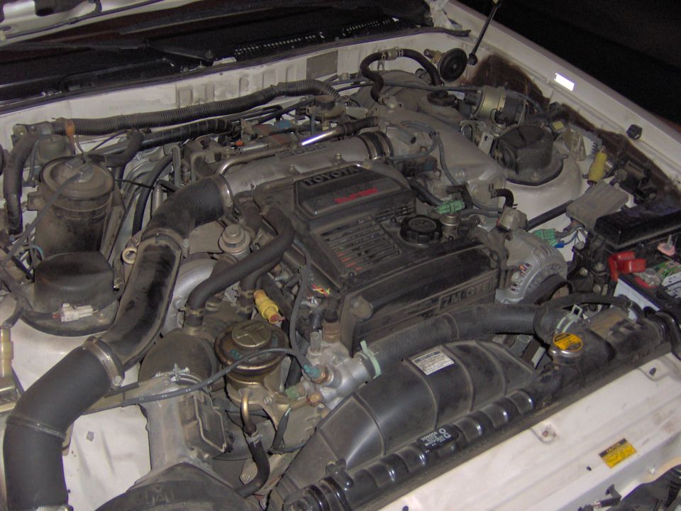 Toyota EFI inline-six engine bay in a white car with intake plenum and black intake tubing