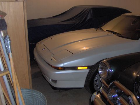 1994 Ford Probe - Silver sports car with pop-up headlights parked in a garage next to another covered vehicle.