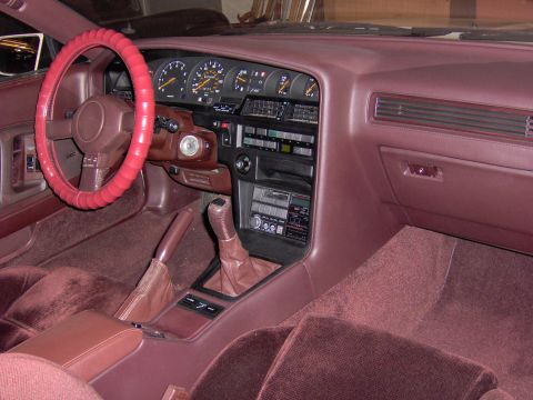 1994 Ford Probe - The interior of a car features maroon carpeting and seats, a red steering wheel cover, and a dashboard with multiple gauges and a radio.