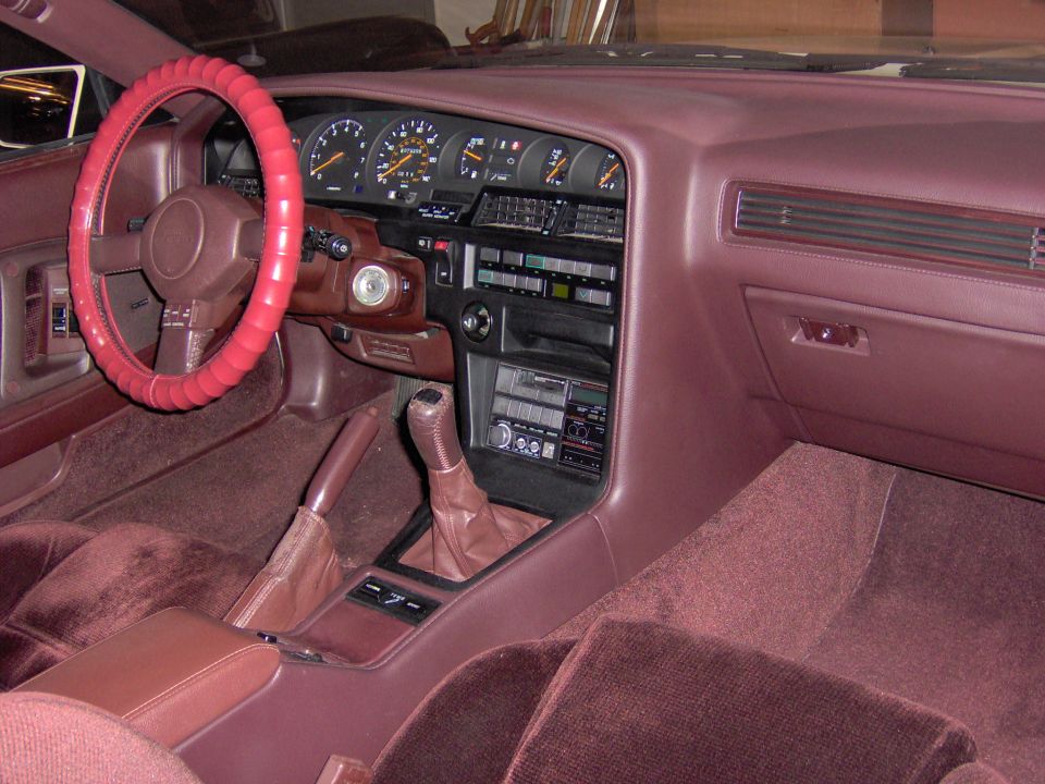 Burgundy 1980s coupe interior with analog gauges, manual shifter and velour seats