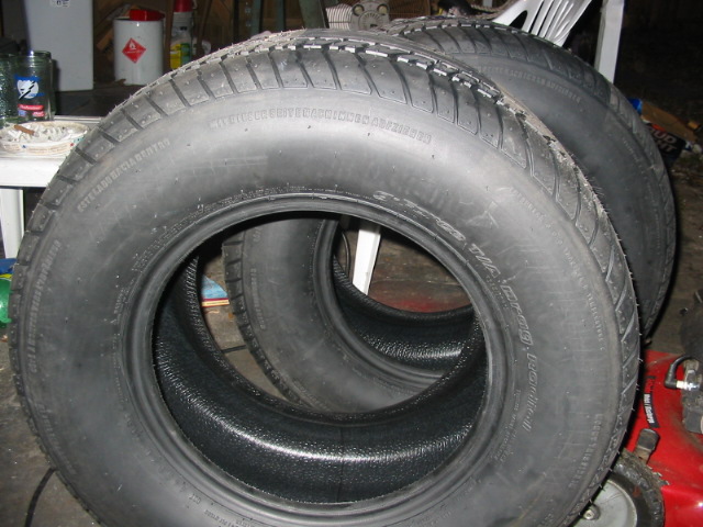Four black tires stacked, with visible tread patterns and sidewall text