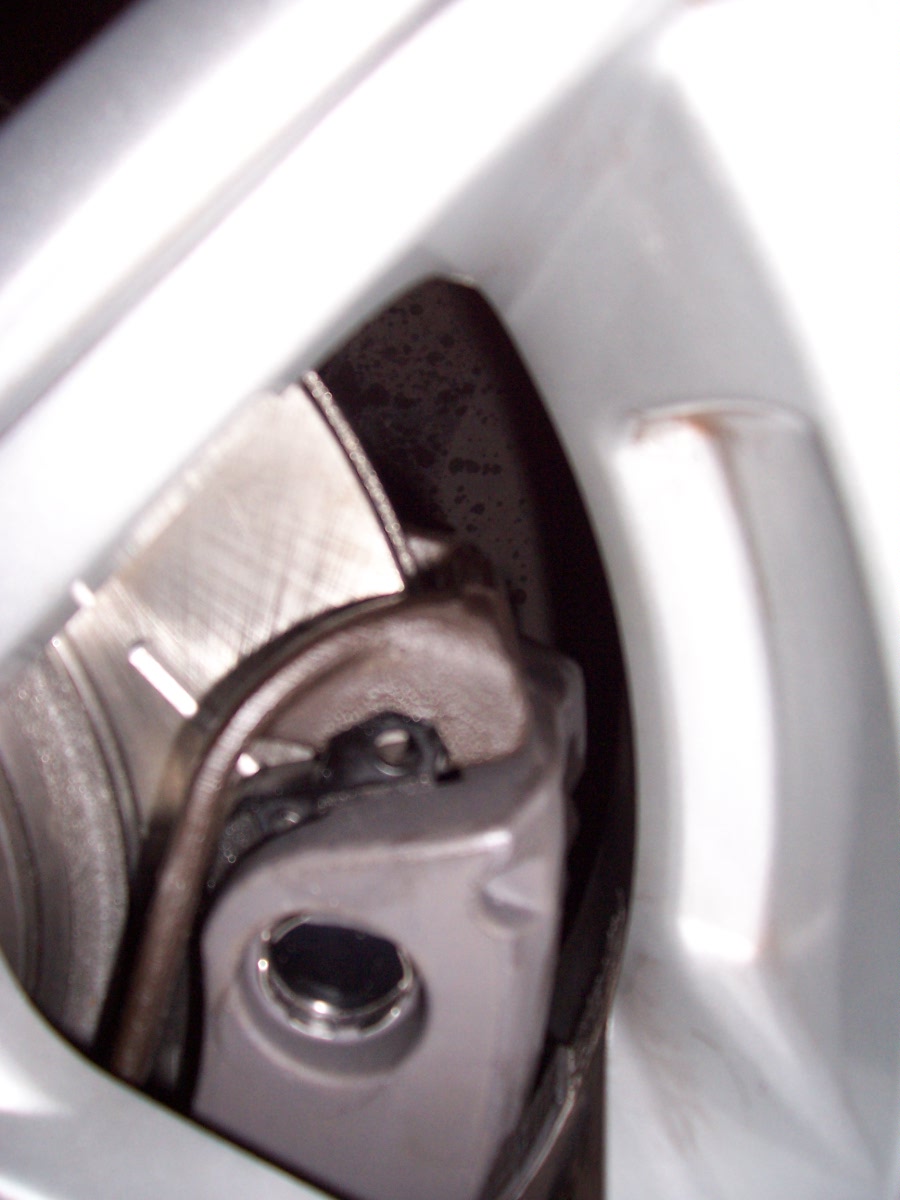 Close-up of a car's brake caliper and rotor assembly, partially obscured by a white wheel rim
