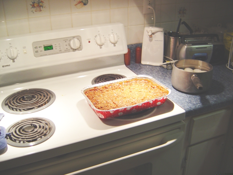 Casserole in foil pan on stovetop next to pot of eggs and kitchen appliances