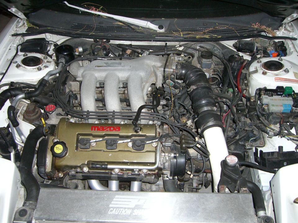 Engine bay with a gold Mazda valve cover and silver intake manifold. Wires and hoses are visible