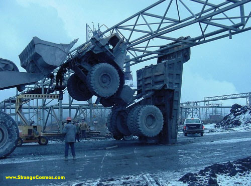 Overturned industrial vehicle in a scrapyard with a white SUV in the background