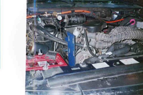 1994 Ford Bronco - The engine bay of a vehicle, showing the battery, hoses, and various engine components.