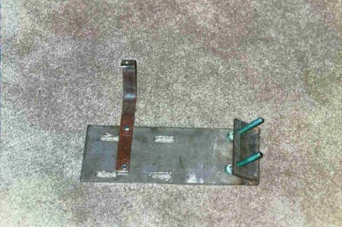 1994 Ford Bronco - A metal bracket assembly with a strap and two green bolts is shown against a carpeted background.