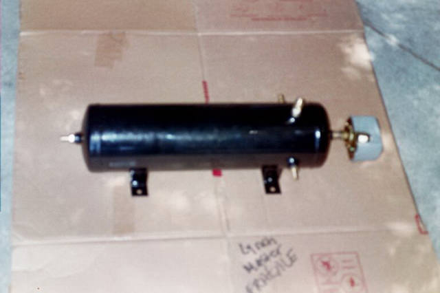 Black cylindrical air tank with mounting brackets and brass fittings on cardboard