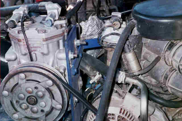 Belt-driven compressor on a blue bracket in an engine bay, alternator at lower right