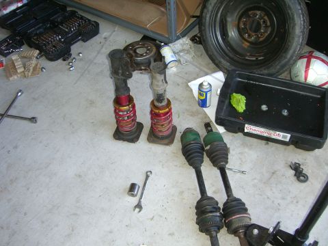 1996 Ford Probe - Car parts including drive axles and suspension assemblies are laid out on a garage floor.