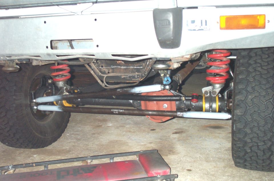 Underside of a lifted vehicle showing red coil springs, track bar and steering linkage