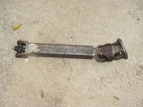 1989 Ford Bronco - A driveshaft component lies on a concrete surface, showing its universal joints and metal construction.