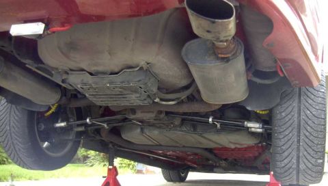 1997 Ford Taurus - Underside rear view of a red car raised on red jack stands, showing an oval muffler with a large chrome-tipped turndown exhaust outlet exit…