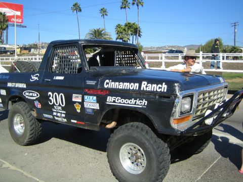 1990 Ford Bronco - dark caged off-road truck lettered Cinnamon Ranch and numbered 300 with BFGoodrich decals sits on a sunny lot among palm trees.