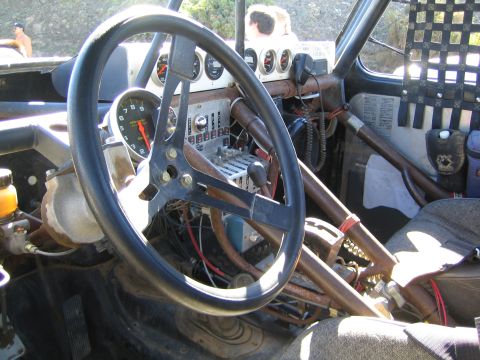 1990 Ford Bronco - stripped interior of an off-road race vehicle with a black steering wheel, mounted tach and gauges, and a dense switch panel inside a roll…