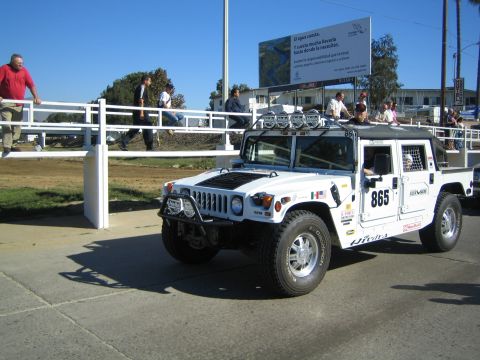 1990 Ford Bronco - white Hummer-style off-road vehicle numbered 865 with a roof light bar and winch sits on pavement near a billboard, with pedestrians in the…
