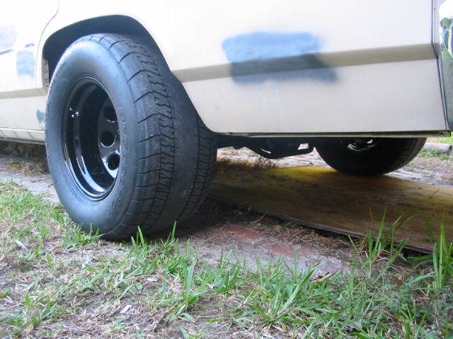 Rear wheel with black rim and drag radial tire on a white vehicle with a blue spray-painted patch on the fender