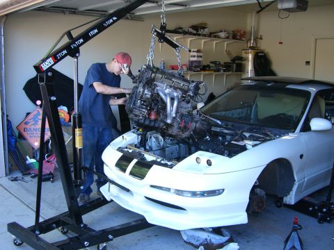 1996 Ford Probe - A mechanic uses an engine hoist to remove the engine from a white 1996 Ford Probe in a garage.