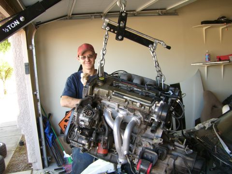 1996 Ford Probe - A person stands by as an engine is hoisted out of a vehicle in a garage.