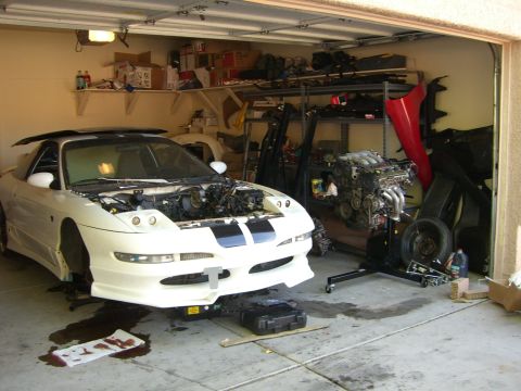 1996 Ford Probe - A white 1996 Ford Probe sits in a garage with its hood open and engine removed, surrounded by spare parts.