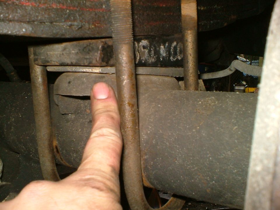 Close-up of a suspension shim being installed under a leaf spring, with the word "BRONCO" visible on a metal component