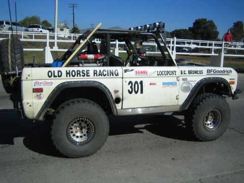 1990 Ford Bronco - Side profile of a white early Ford Bronco off-road racer numbered 301 with 'Old Horse Racing' and 'Locopony' lettering and a roof light bar.