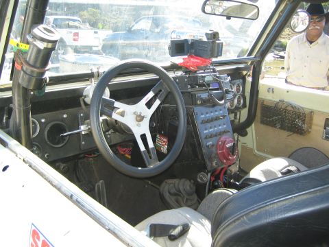 1990 Ford Bronco - interior of an early Bronco race vehicle showing the steering wheel, dash switches and instruments, with a mustachioed man visible through…
