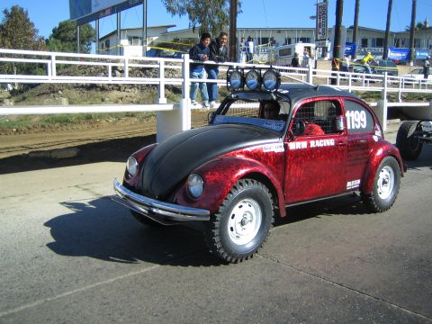 1990 Ford Bronco - red-and-black Volkswagen Beetle built as a Baja off-road racer, marked 1199 and MRM Racing, sits on a paved lot with a roof light bar.