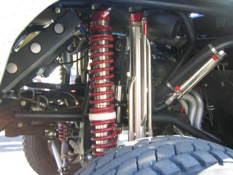 1990 Ford Bronco - close-up of an off-road race truck's rear suspension shows red coilover springs, a polished bypass shock and the rear tire.