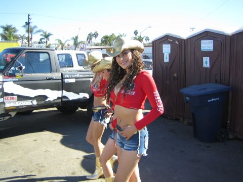 1990 Ford Bronco - Two women in red tops, denim shorts and cowboy hats pose at an outdoor event near pickups and portable toilets.