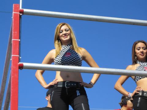 1990 Ford Bronco - blonde woman in a black-and-white checkered crop top poses with hands on hips on a red-railed platform under a blue sky.