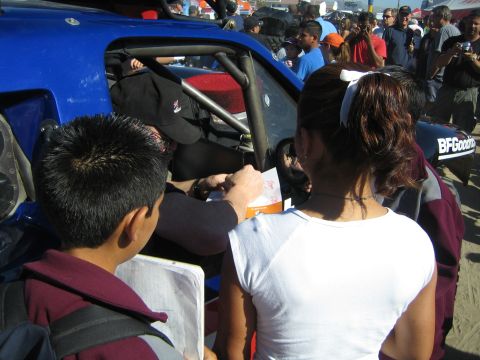 1990 Ford Bronco - Spectators gather closely around a blue tube-frame off-road race vehicle, with one person signing a paper near the cockpit.