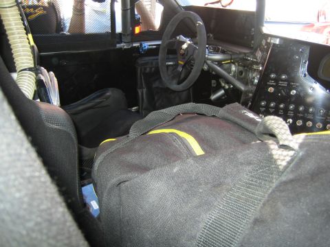 1990 Ford Bronco - Stripped race-car interior with a removable steering wheel, roll cage, racing seat and a switch panel, partly covered by a black bag.