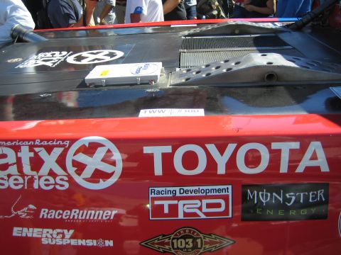 1990 Ford Bronco - Rear deck of a red Toyota off-road race car covered in sponsor decals including TRD, Monster Energy and Etx Series, viewed in a crowd.