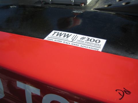 1990 Ford Bronco - racing sponsor decal reading 'TWW #300 Moss Brothers 2005 Score Baja 1000 Adventure' on the black-and-red body panel of a vehicle.