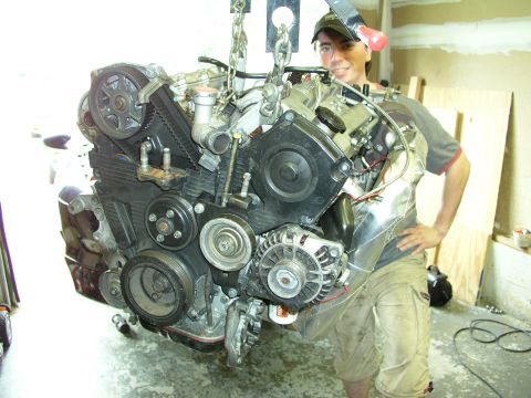 1996 Ford Probe - A person stands by as a car engine is hoisted by chains in a garage setting.