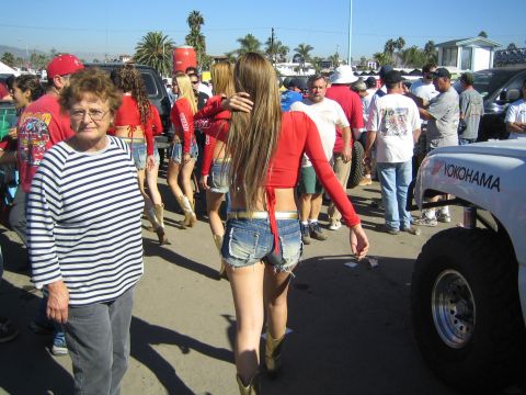 1990 Ford Bronco - crowded outdoor event with promotional models in red tops and denim shorts walking past spectators and a large Yokohama-branded off-road ti…