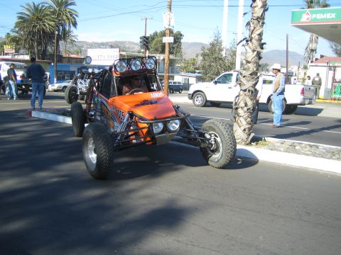 1990 Ford Bronco - orange single-seat off-road sand rail buggy with roof-mounted lights parked on a street near a Pemex gas station and palm trees.